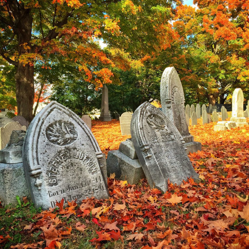 Pointy-topped gravestones from the 1800s set among red and orange autumn leaves.