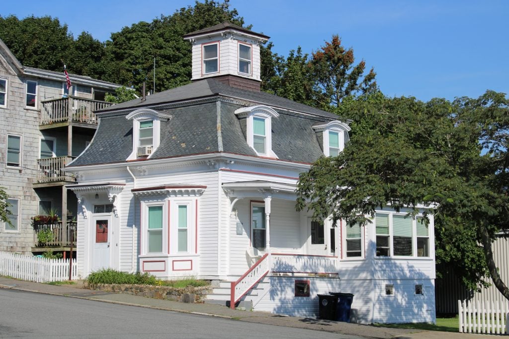 The house from Hocus Pocus: a short, chubby white Victorian house with red trim. There is a bay window on the first floor next to the red front door, and a small porch. The second floor has windows peeking out of the concave curved roof. Out of the top of the roof pokes a tiny square lookout with windows on each side, perhaps big enough for a desk but nothing else. It's the only part of the third floor.