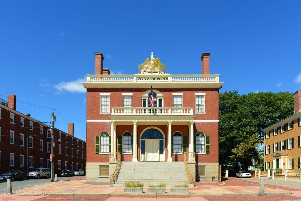 A red brick building with white columns and white balcony. It reads CUSTOM HOUSE on top beneath a sculpture of an eagle.