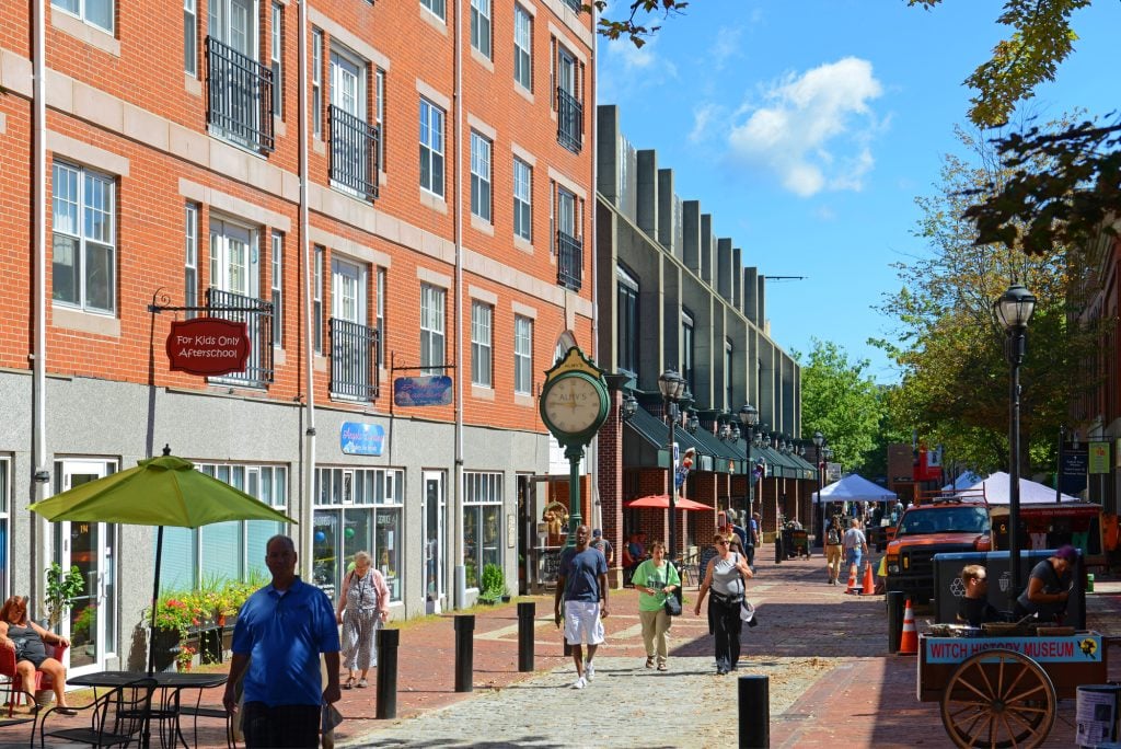 People walking down a cobblestone street surrounded by red brick buildings, some containing shops.