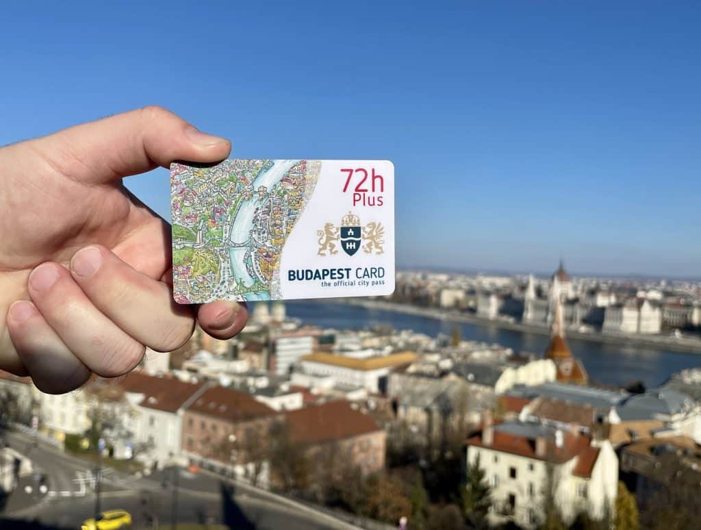 A male hand (Kate's knuckles are not that hairy, she swears) holding a 72-hour Budapest Card in front of the skyline, including the spiky Parliament building.