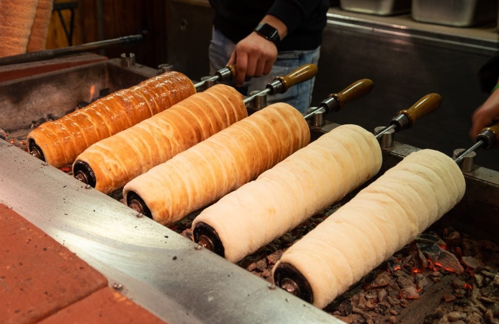 Five roasting chimney cakes of various doneness rotating on a grill.