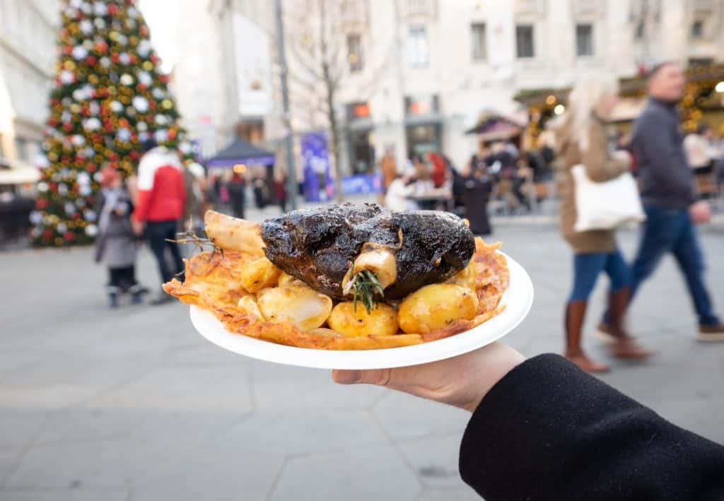 Charlie's hand holding a lamb shank stuffed with rosemary on top of roasted potatoes and a potato-onion pancake.