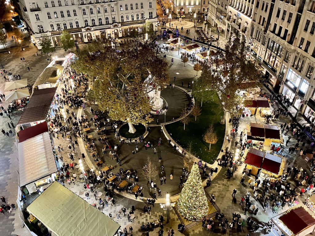 An aerial view of the oval-shaped Christmas Market on Vorosmarty Square, stalls along the edge and a park in the center.