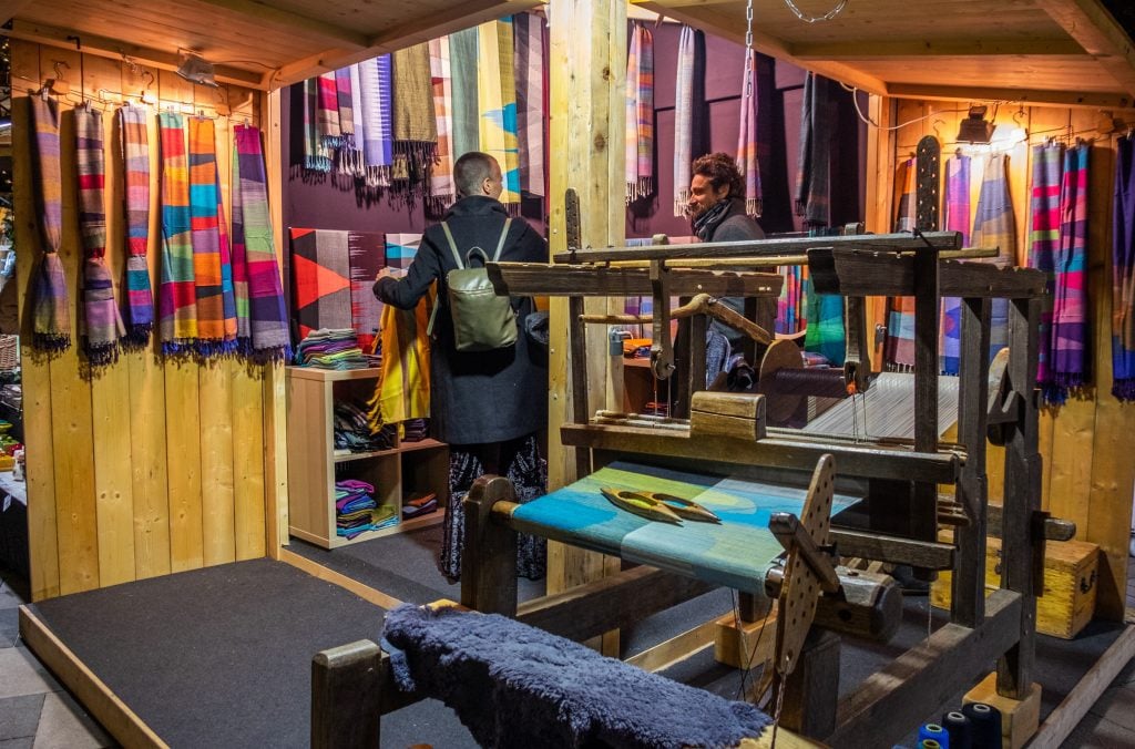 A wooden stall filled with brightly colored woven scarves, with an actual wooden loom in front.