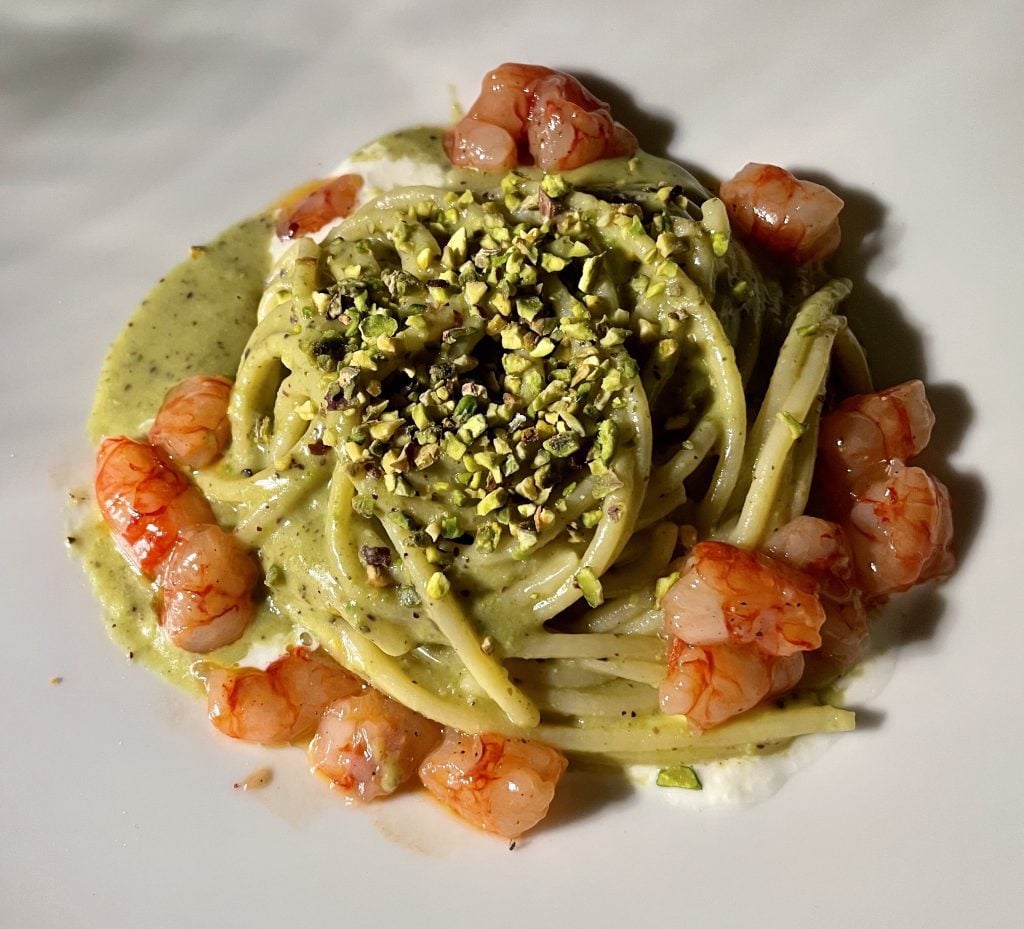A plate of pasta in pistachio pesto, stracciatella cheese, and red shrimp that look almost raw.