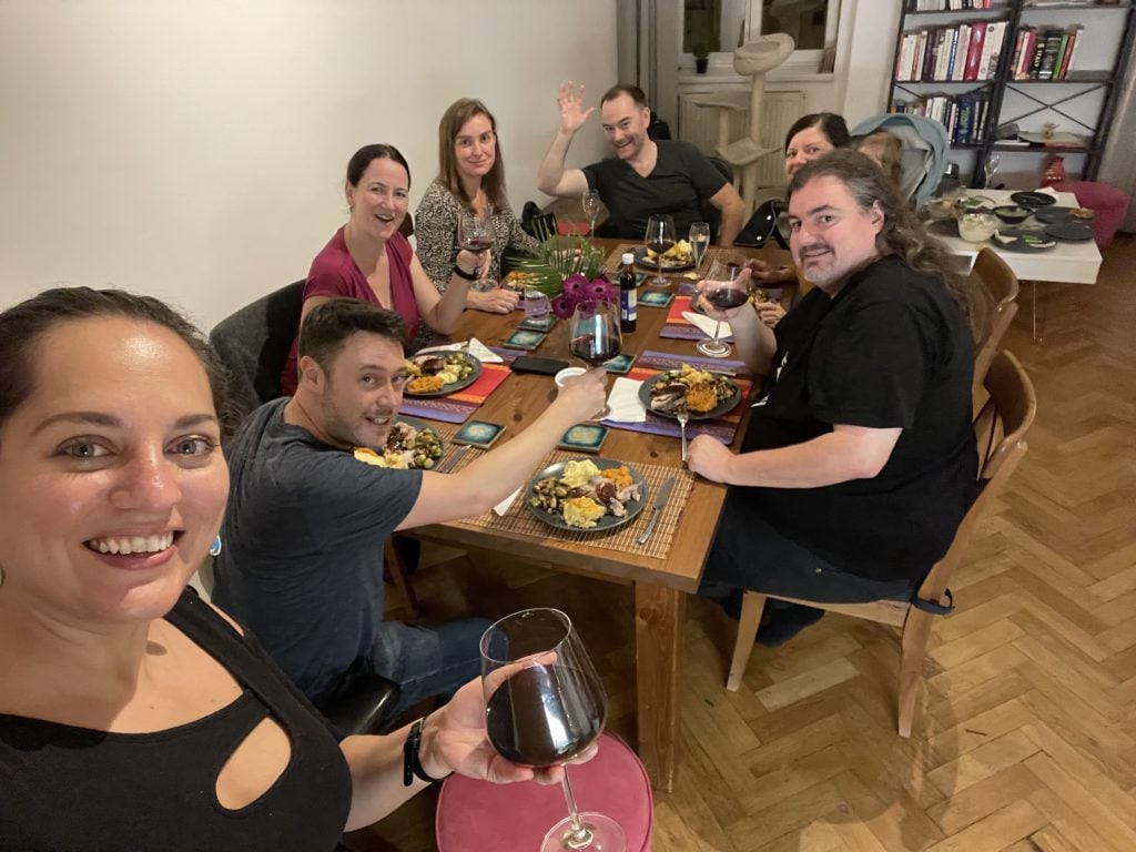 Kate taking her selfie with a table full of seven friends behind her smiling at the camera on Thanksgiving.