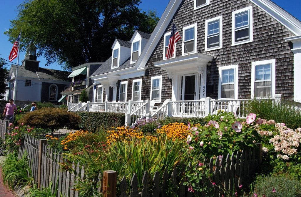 A wooden shuttered house with a big overgrown garden in front.