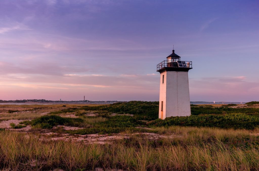 The white Wood End Lighthouse during a purple sunset, sand dunes all around.