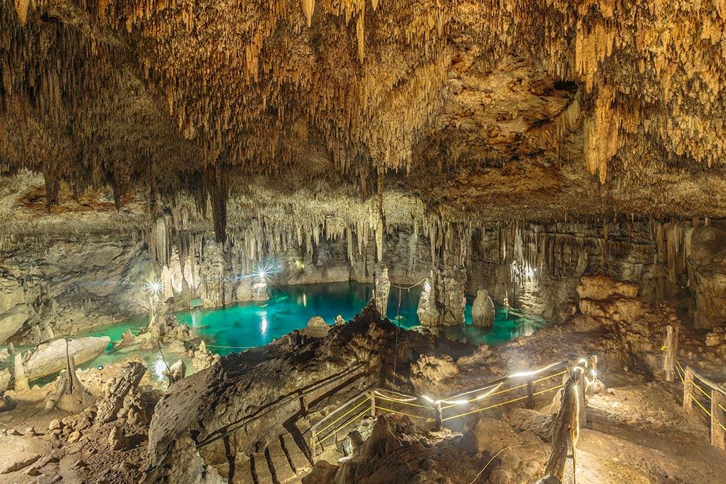 An enormous cave cenote with lots of stalactites and stalagmites surrounding a bright turquoise pool.