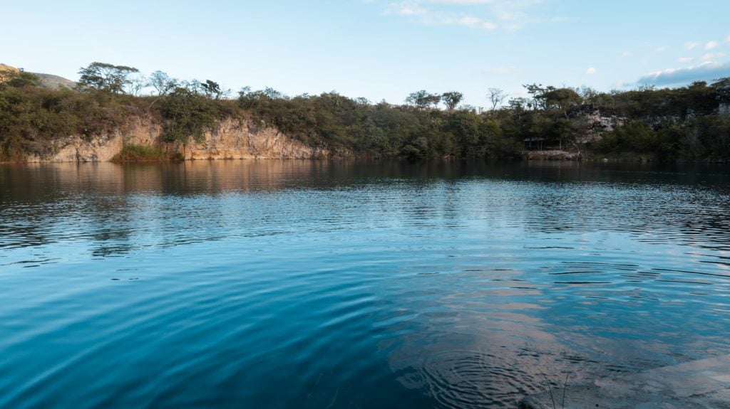 A dark blue open cenote that looks like a lake, surrounded by short gray cave walls.