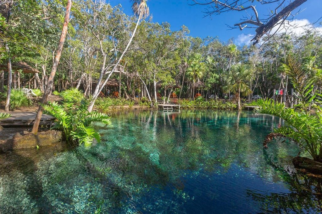 A clear green cenote that looks like a lake, surrounded by lush vegetation.