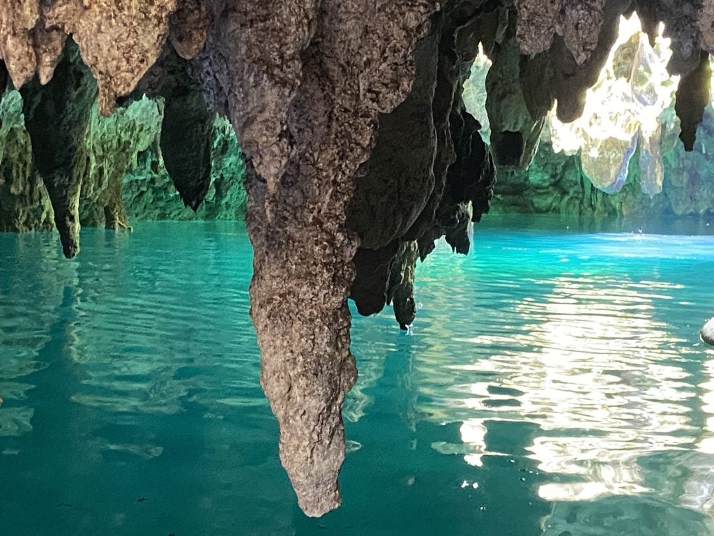 Enormous fat stalactites hanging above bright turquoise water in a cenote.