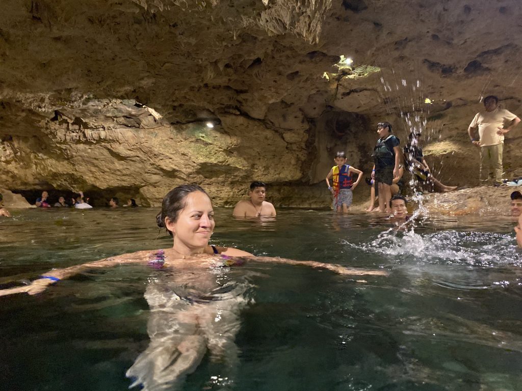Kate swimming in an indoor cave cenote with lots of people packed into a small space. She makes a face as a kid splashes her with water.