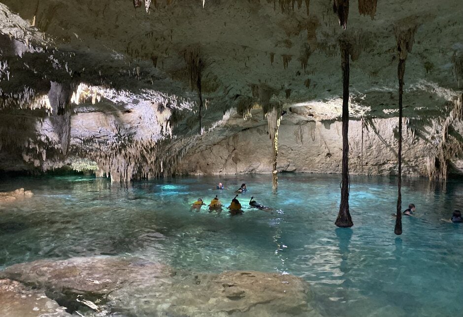 A group of snorkelers snorkeling inside the bright blue water inside a cave with lots of stalactites.