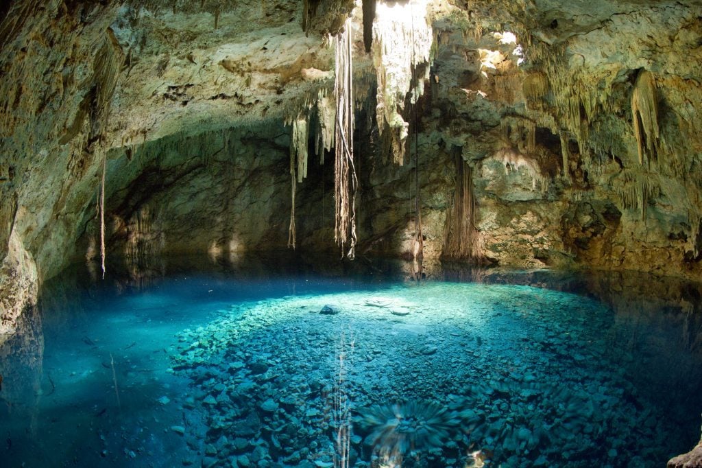 A cenote inside a cave with bright aqua water.