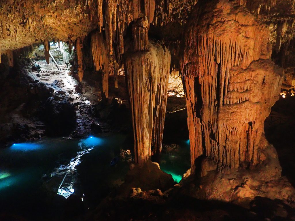 A cave with monstrous-looking giant stalactites and electric blue water.