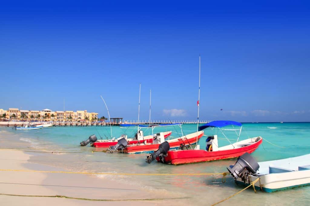 Red fishing boats parked on the edge of the beach, in the clear turquoise water.