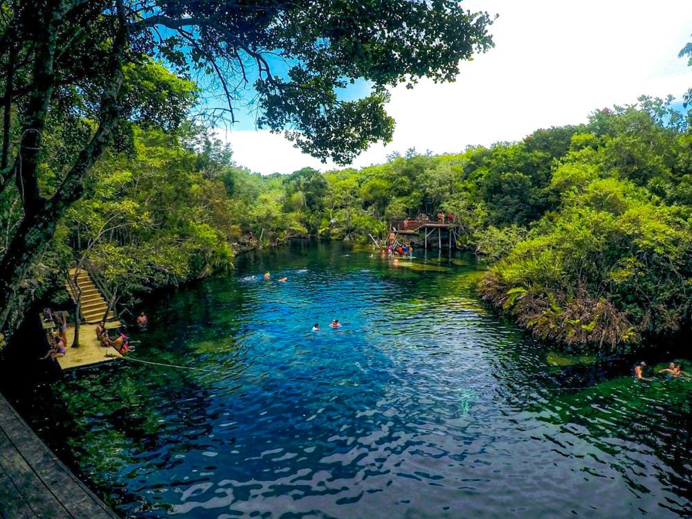 A cenote that looks like a large open lake, with some wooden platforms on the edges, in the middle of a jungle.