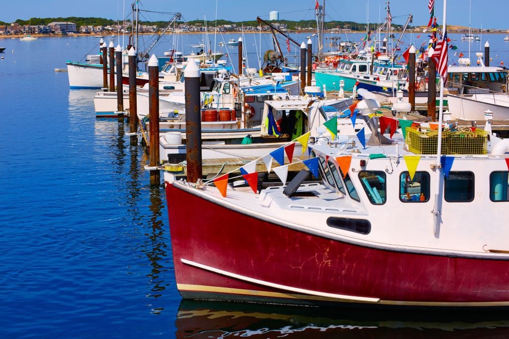 Several small fishing boats lined up, some of them with brightly colored flags hanging from them.