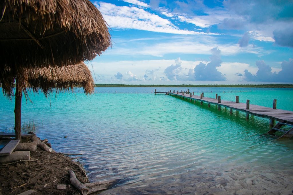 A wooden deck leading across a neon turquoise cenote that looks more like a lake.