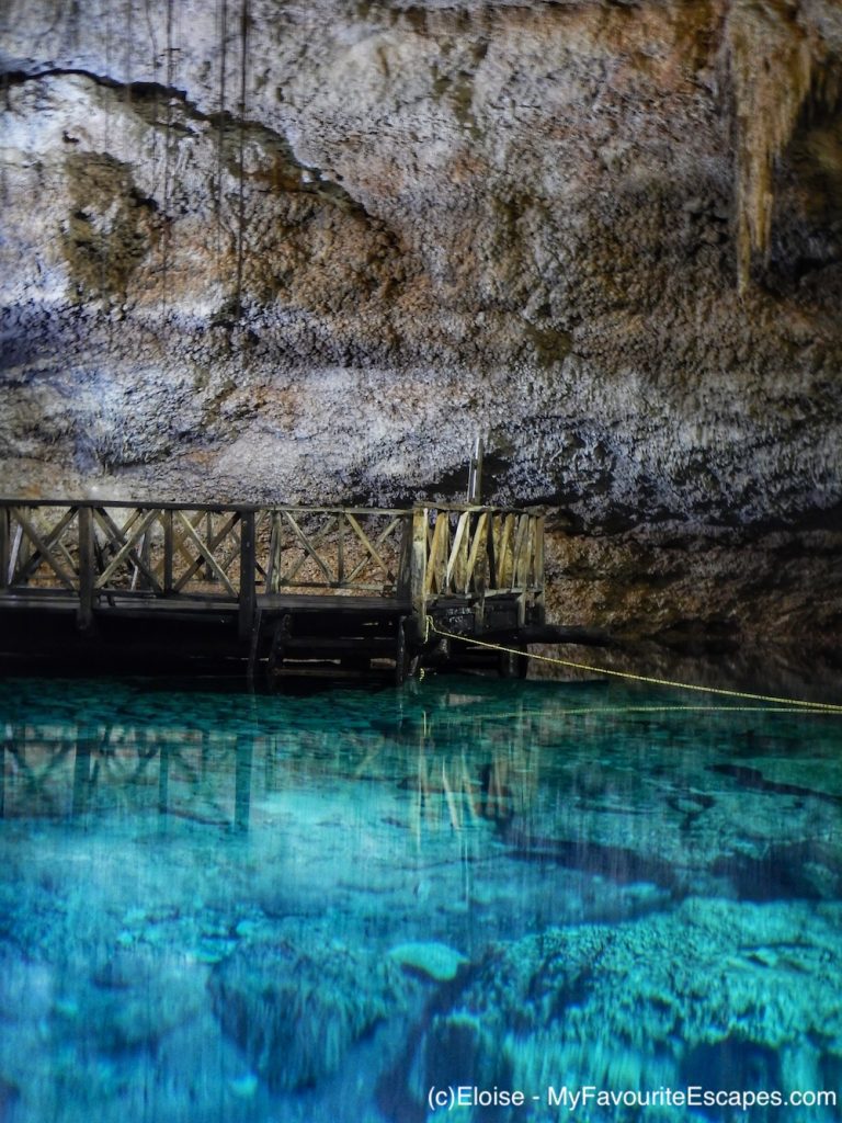 A wooden platform looking over a mirror-like turquoise cenote.