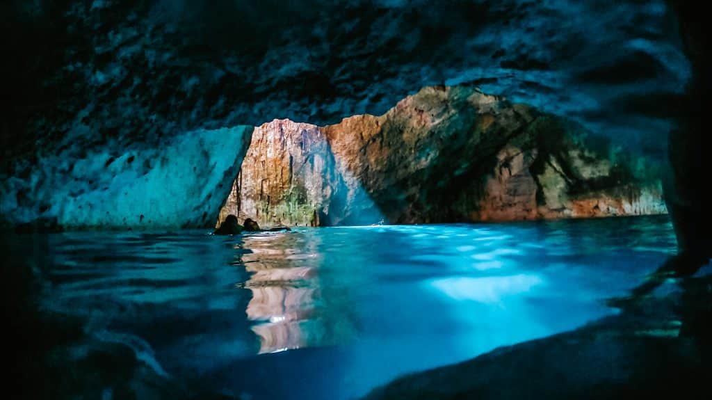 The inside of a cave cenote with bright neon blue water.