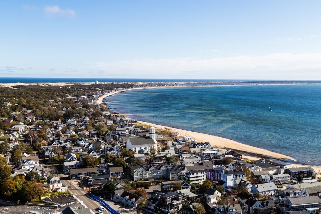 An aerial view of Provincetown, lots of small buildings and a curved beach along the calm blue bay.