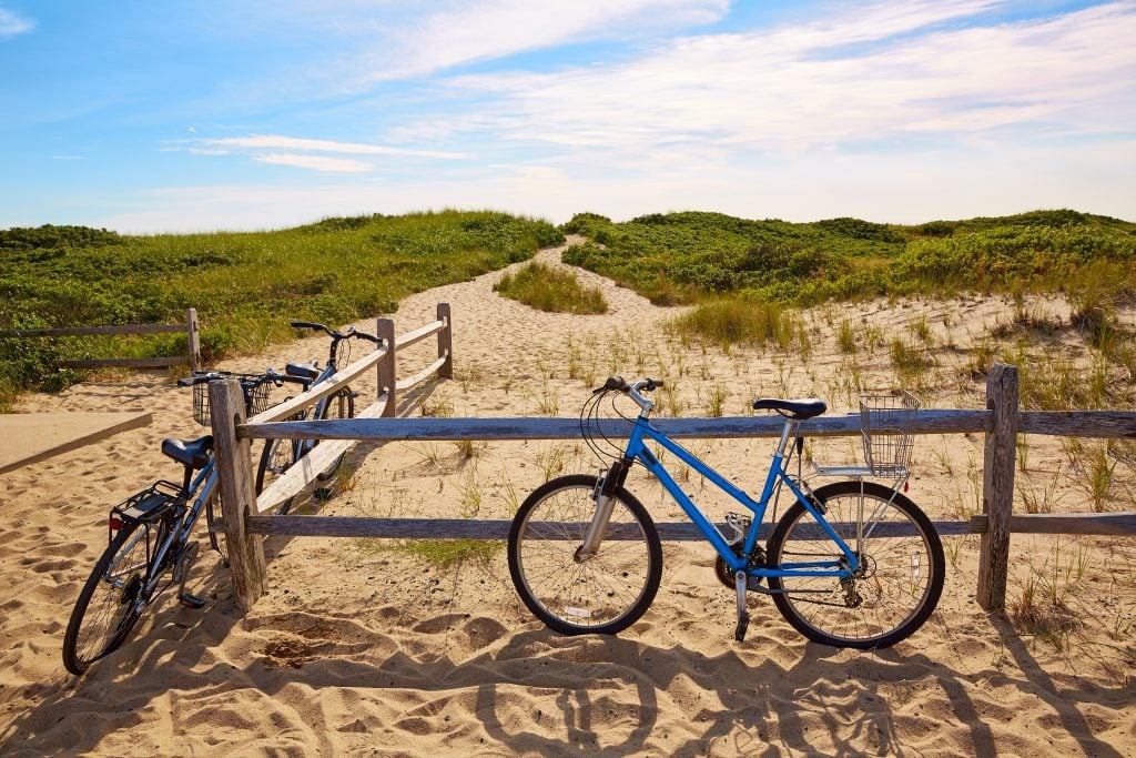 A bike parked next to a wooden fence in front of a sand dune.