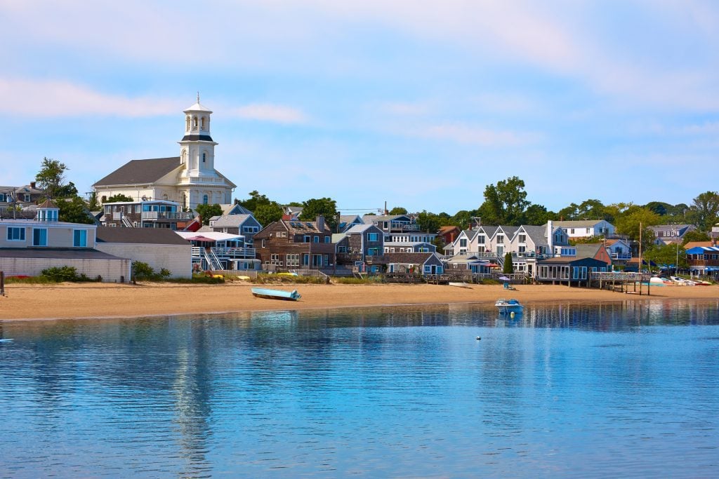 Provincetown buildings and a beach in front of a calm blue bay.