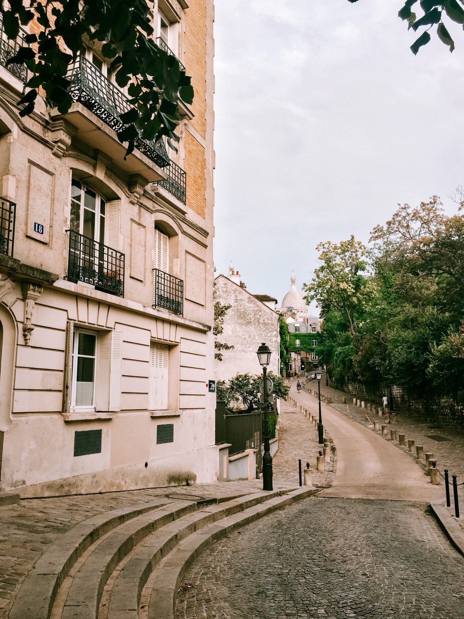 An angled view of a cream colored building on Rue de l'Abreuvoir in Paris, with a walkway in front and grass and trees on the right side of the path