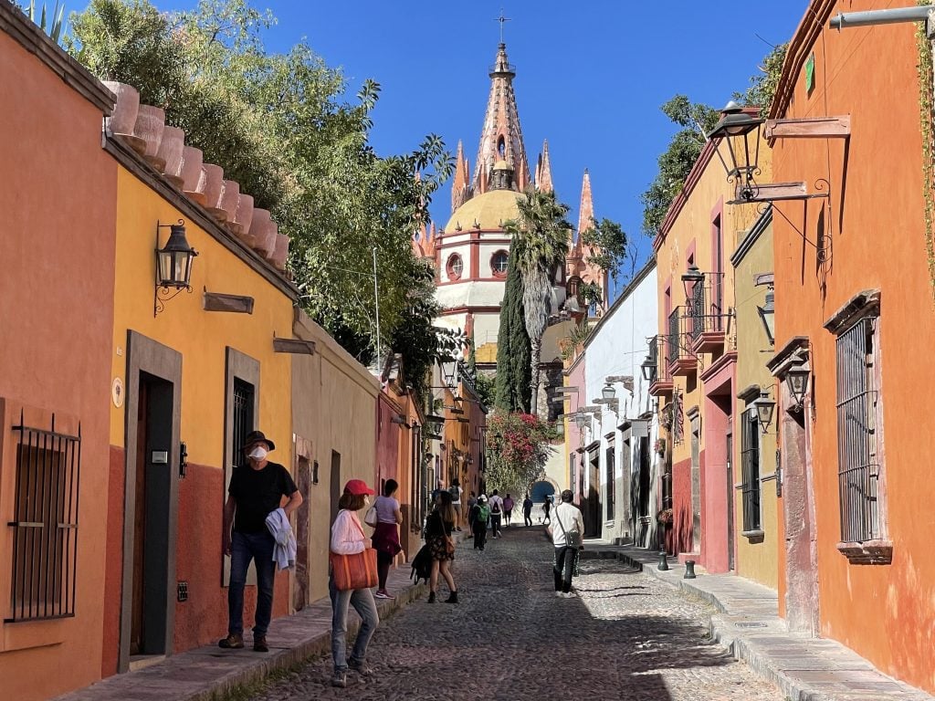 A spiky yellow and red church at the end of a brightly painted cobblestone street in San Miguel.