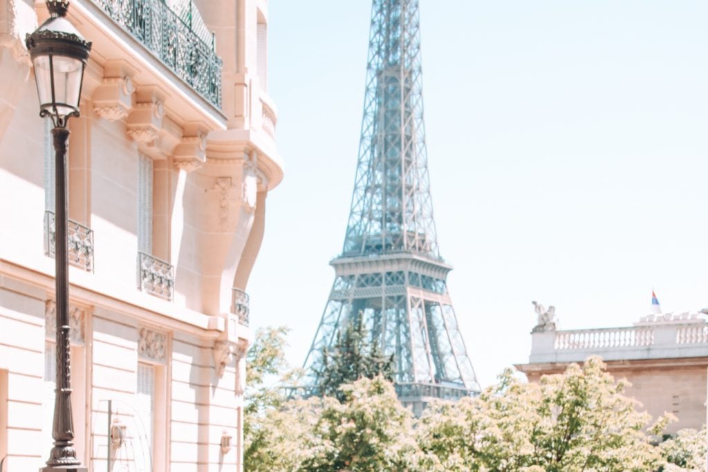 A partial view of the Effiel tower over the treetops from Avenue de Camoëns, with a building on the lefthand side