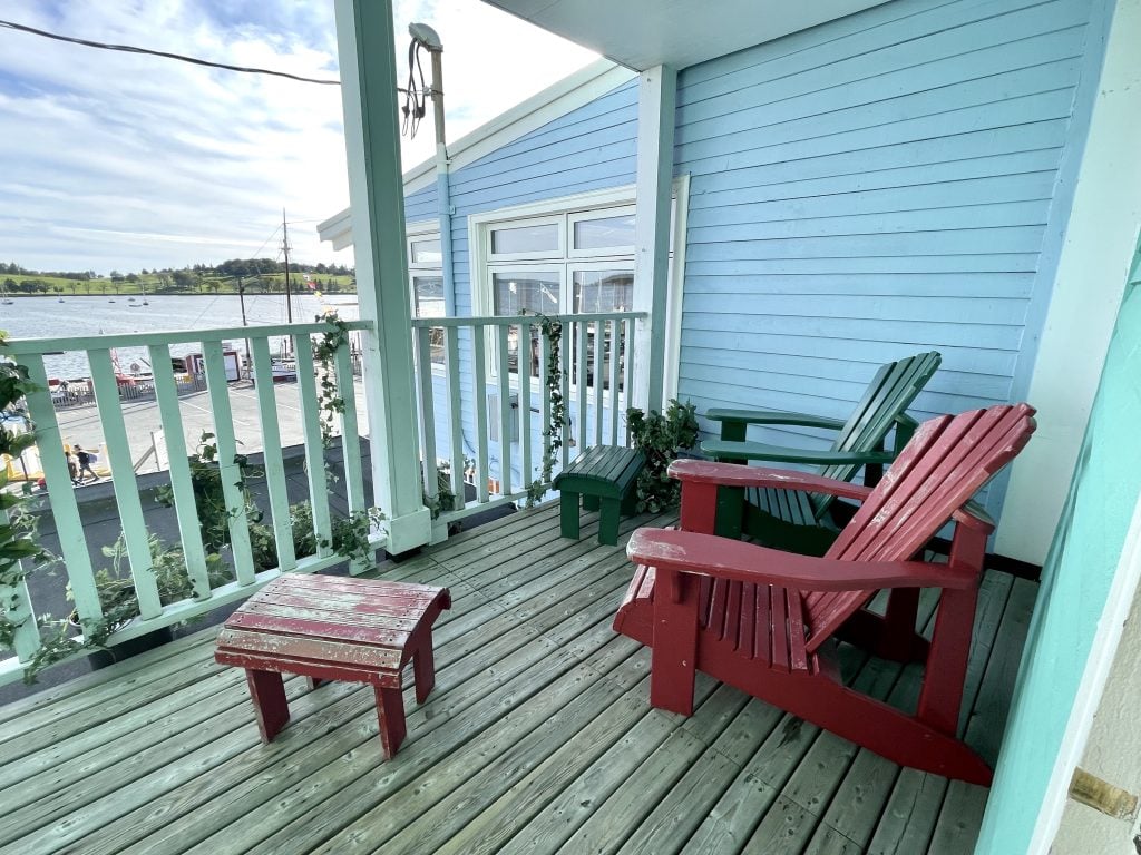 A deck with two weathered Adirondack chairs overlooking a parking lot and the water beyond that.