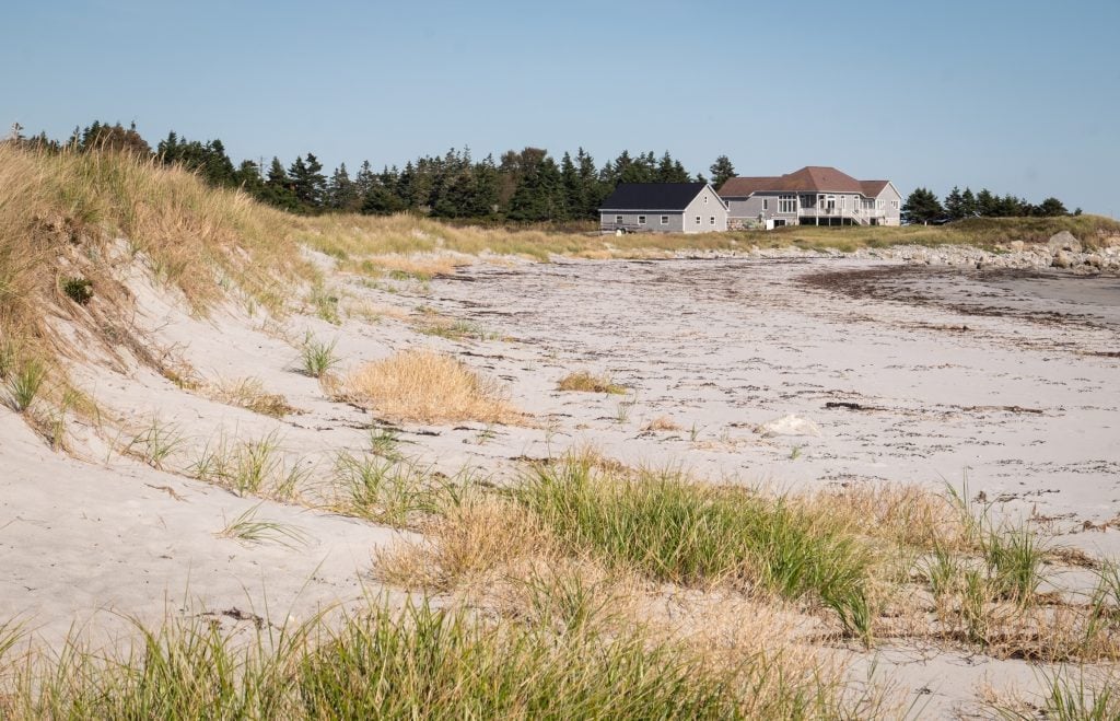 Huge grassy sand dunes, and a large beach cottage in the distance.
