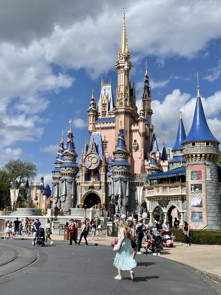 Cinderella's castle at the Magic Kingdom, Disney World, all gray and pink with pointy blue towers, covered with tons of gold trim, swirling gold ribbons, and a giant 50 on the front.