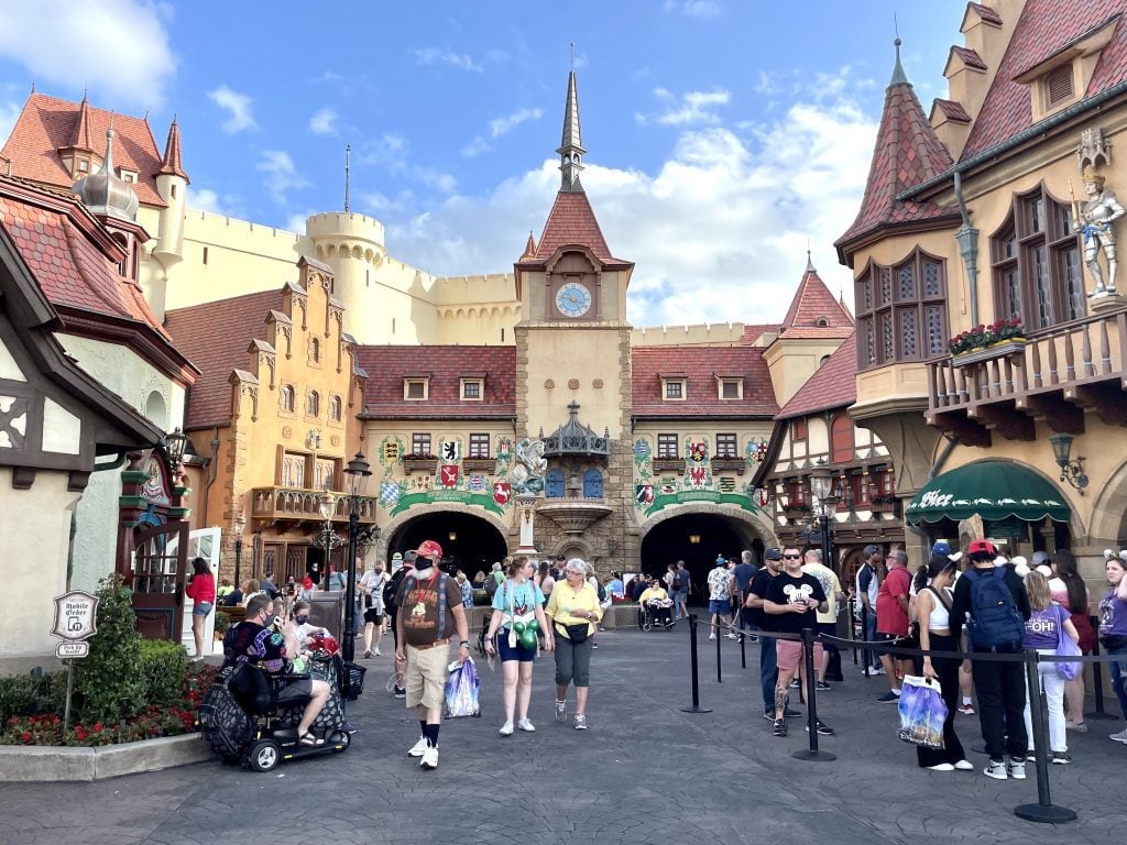 The Germany Pavilion with warm-colored crenellated homes, clock towers, Tudor-style wooden houses in dark brown and white, and tons of people waiting in line.