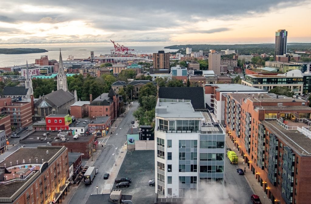 The city landscape of Halifax taken from a high view. You see tall buildings, church steeples, and the harbour, all under gray-pink light.