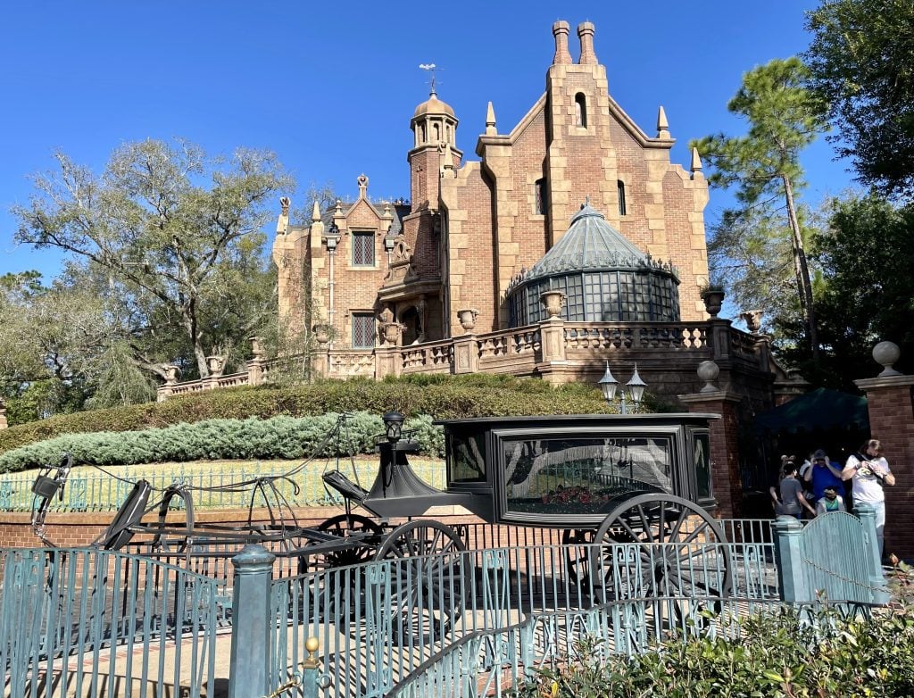 The haunted mansion, with a horse-drawn hearse (and an invisible horse pulling it) in front of a red brick spooky looking building.