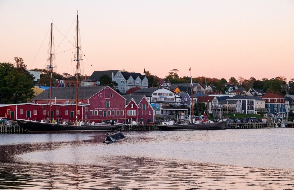 Lunenburg's waterfront at sunset, a pink sky ahead, the Bluenose tall ship and the bright red Fisheries Museum.