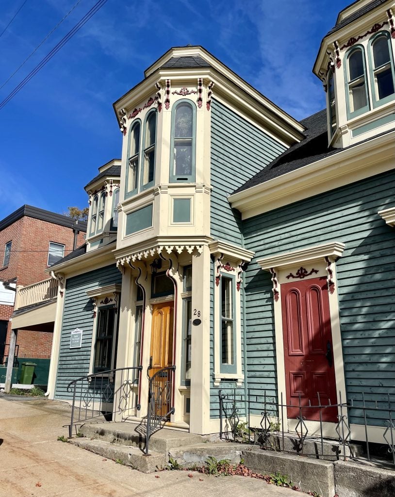 A green and yellow Victorian crenellated house that has a tiny bump on the second floor that sticks out above the door about 50 cm or so.