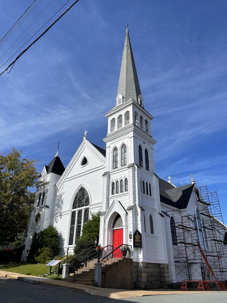 A tall white church with a red door, and lots of tall windows that point upward.