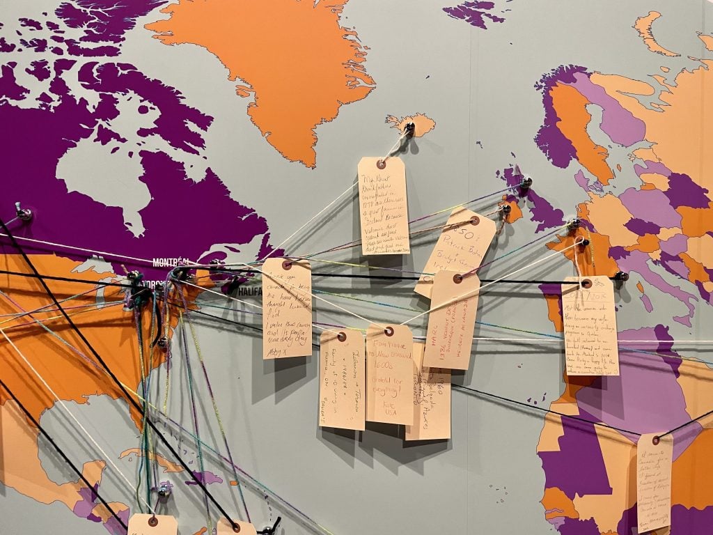 A wall map where people put strings to show their family's journey to Canada and cards telling the stories.