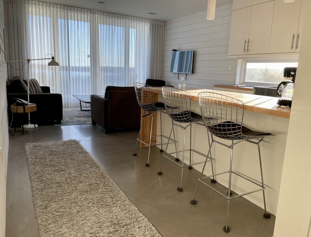 A simple white modern kitchen leading back to a living room area with gray couches.