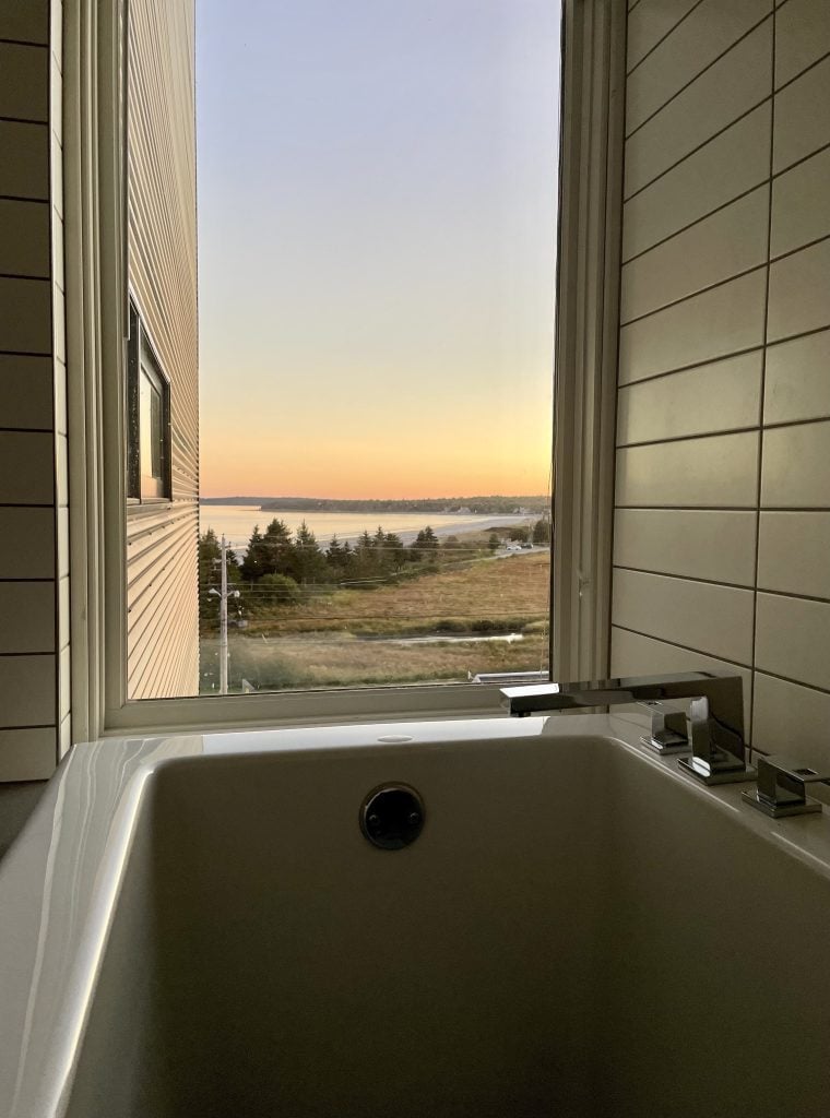 Viewpoint from sitting in the bathtub: a beach in the background underneath a sunset.