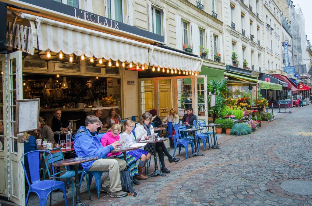 A family sits outdoors at a cafe called L'Eclair in front of a shop-lined cobblestone street.