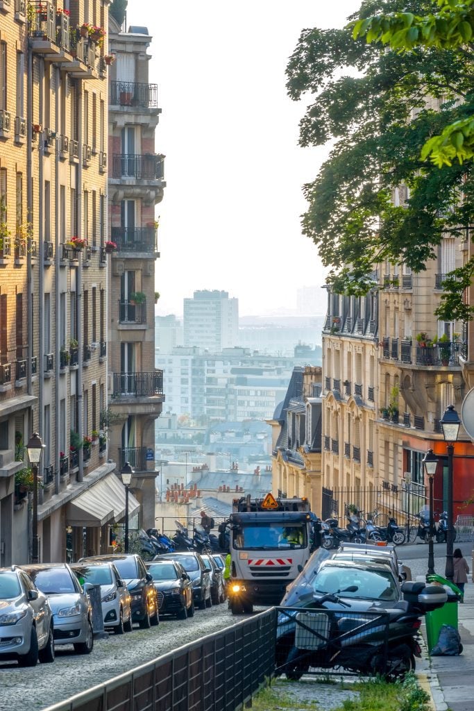 A tall, narrow, steep street with lots of traffic and views of the city below.