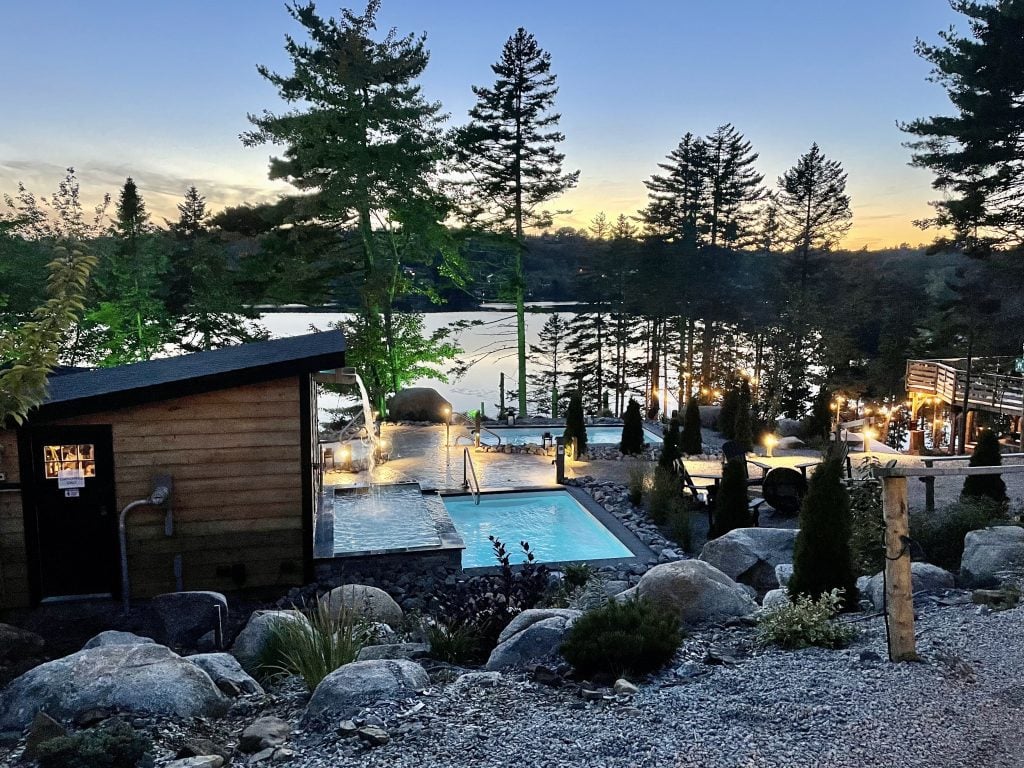 Another view of the pools among the trees in front of the lake, as the sun sets and lights are lit around the surroundings.