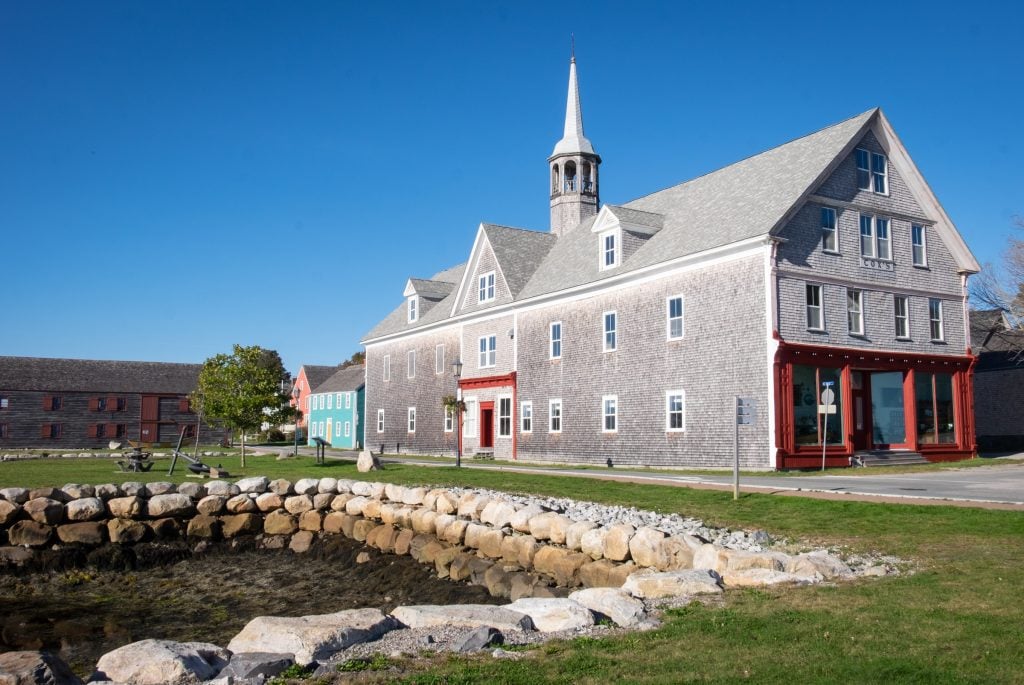 An old-fashioned gray shingled building with a steeple on top.