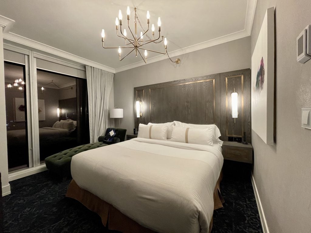 A big white bed in a luxurious hotel room, with a gold chandelier, decorated in dark gray and gold.